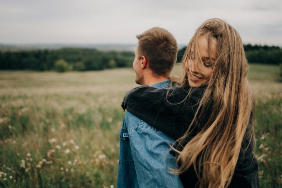 A woman embracing a man from behind in a green meadow
