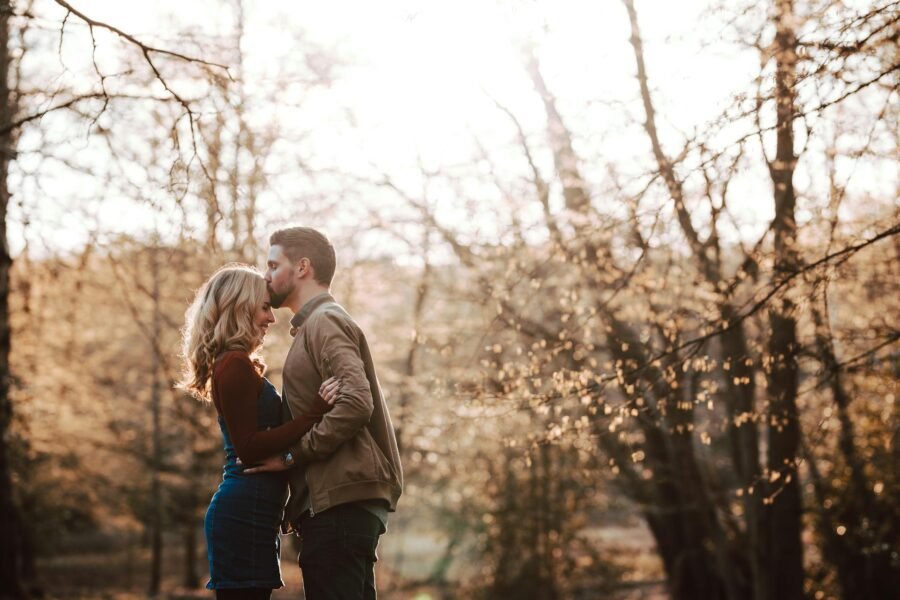 A couple in a forest during fall, men kissing the woman on her forehead